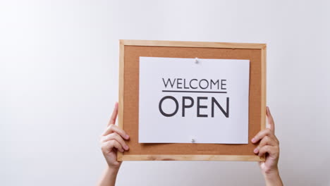 woman's hand shows the paper on board with the word welcome open in white studio background with copy space