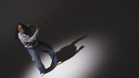 Looking-Down-On-Studio-Shot-Of-Young-Woman-Dancer-Wearing-Hoodie-Dancing-In-Spotlight-In-Slow-Motion-2