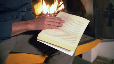 man finds solace and relaxation as he immerses himself in a book, while the cozy warmth of a cabin fireplace dances in the background, creating a comforting and serene atmosphere