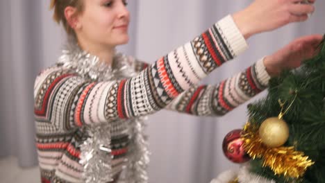 Young-happy-woman-decorating-a-Christmas-tree-taking-a-silver-star-and-hanging-it-on-the-top-of-the-tree.-Slow-Motion-shot