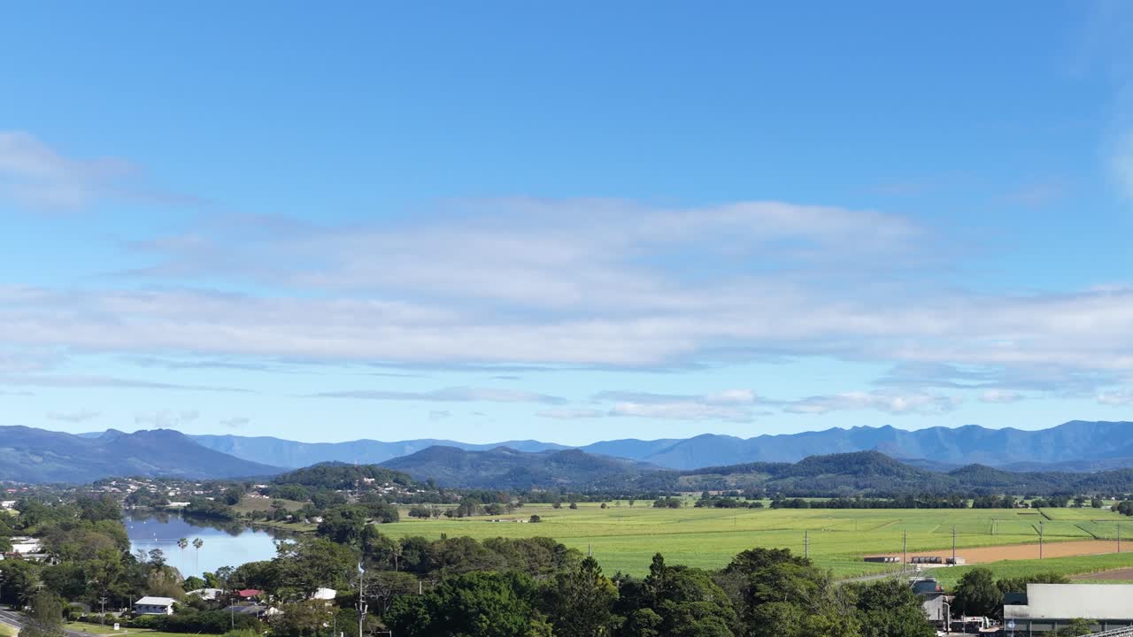 Aerial view of Murwillumbah's sugar mill, lush fields, and distant mountains under a bright blue sky