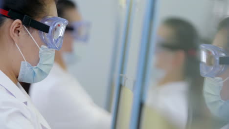 scientists in lab coats wearing safety glasses goggles dropper and chemical or test sample in beaker or test tubes working in biotechnology laboratory