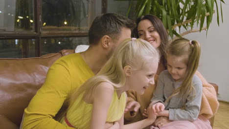 happy family tickling each other and having fun while sitting on sofa at home