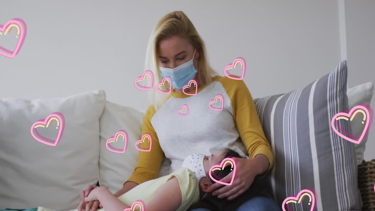 코카시안 여성과 그녀의 딸이 소파에서 놀고 있는 얼굴 마스크를 착용하고 있는 심장의 애니메이션