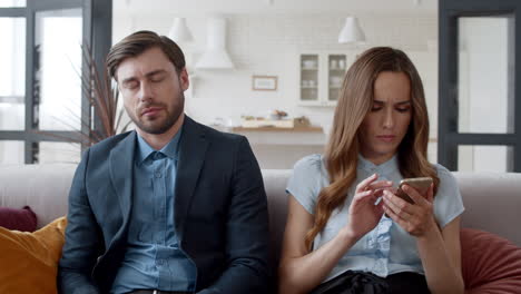 Young-couple-sitting-on-sofa-in-modern-room.-Tired-man-sleeping-on-couch