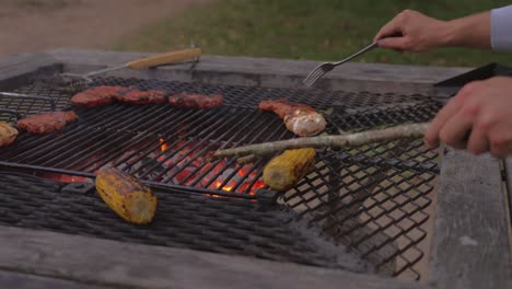grilling steak and corn on a rustic barbecue grill outdoors with a hand turning the food