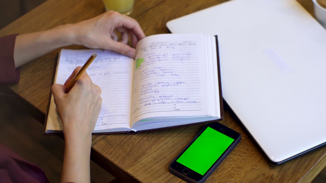mujer de negocios usando un teléfono inteligente y hace notas en un cuaderno en una cafetería. teléfono inteligente con pantalla verde