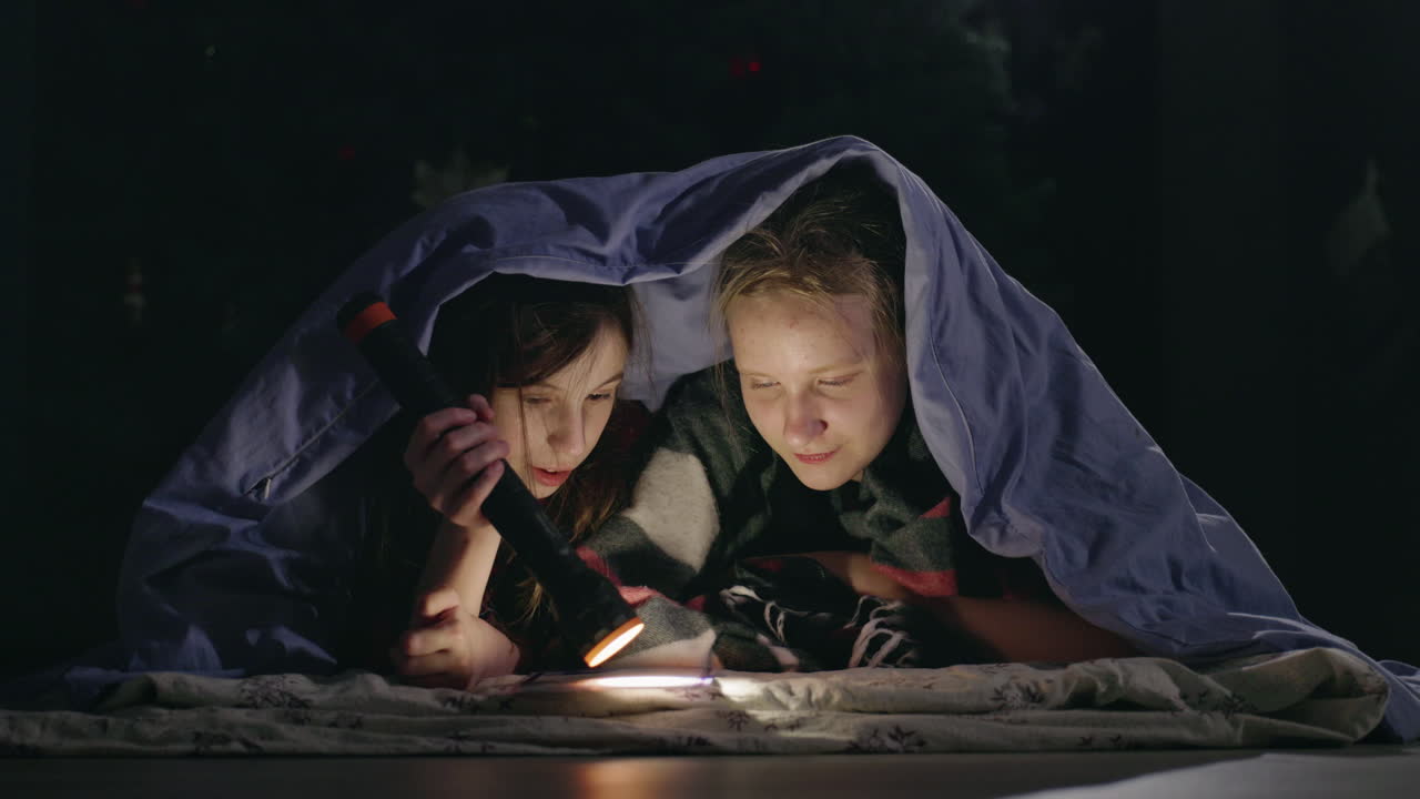 Children under blanket with flashlight at night