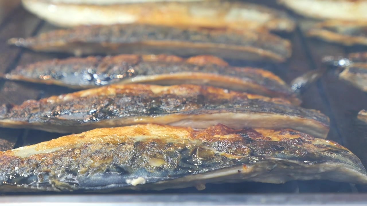 Filetti di sgombro sfrigolanti che grigliano su un barbecue caldo.