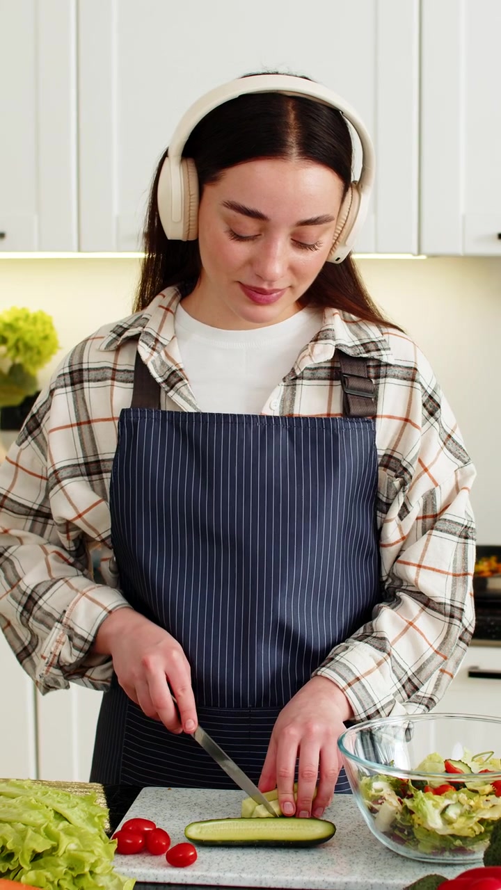 Giovane donna che affetta pomodori e cetrioli aggiungendoli all'insalata per un'alimentazione vegetariana sana in cucina