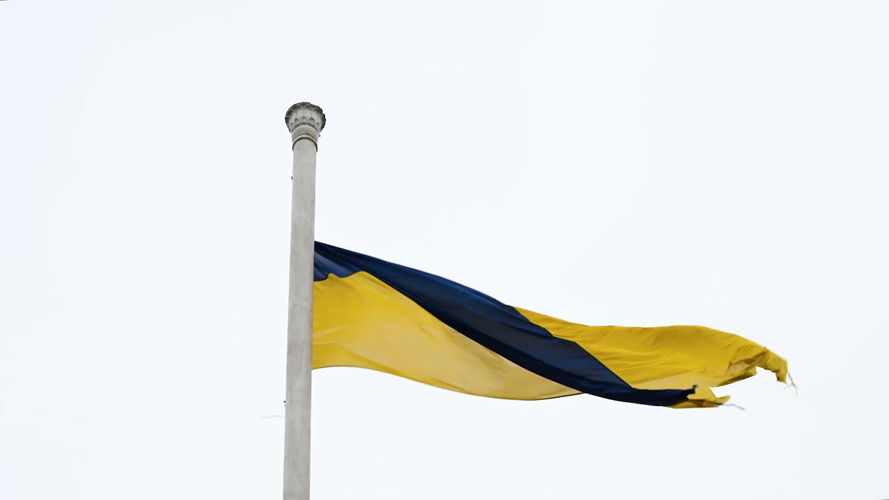 Ukrainian flag seen waving atop a large post, on a cloudy day, showcasing the flag as it interacts with the wind.