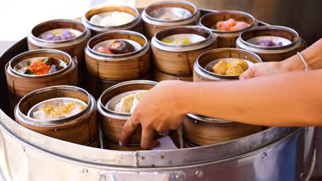 Hands choose dim sum from a steaming basket, showcasing a variety of dumplings in a vibrant, well-lit setting