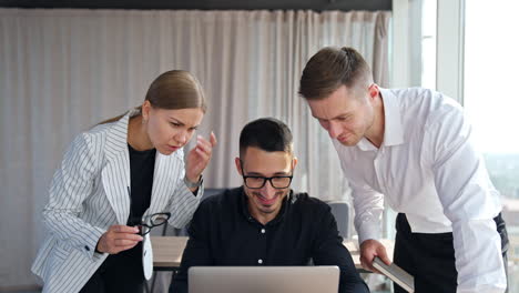 colleagues solving task cooperating at work. three diverse employees look at one laptop screen discussing a problem, being positive.