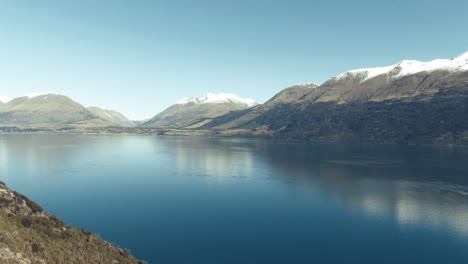 drone pan over glacial lake surrounded by mountains in winter new zealand