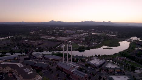 Bend-Oregon-Sunset---Rising-Drone-Shot-of-Old-Mill,-Deschutes-River-and-Cascade-Mountains-in-the-Evening-