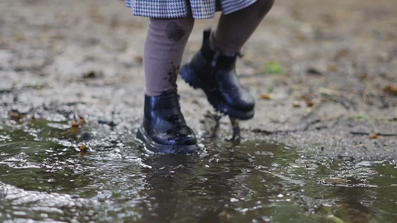 Toddler splashing her black boots in the big muddy puddle, autumn forest