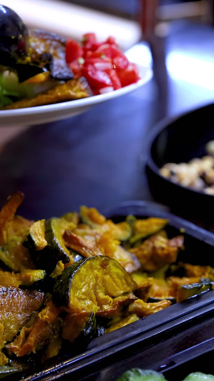 Primo piano di un commensale che usa le pinze per servirsi zucca arrosto a un luminoso buffet di insalate.