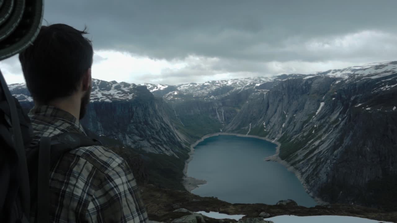 mochilero masculino en la cima de la montaña disfrutando de impresionantes vistas al mar con nieve en la cima durante el día nublado en noruega