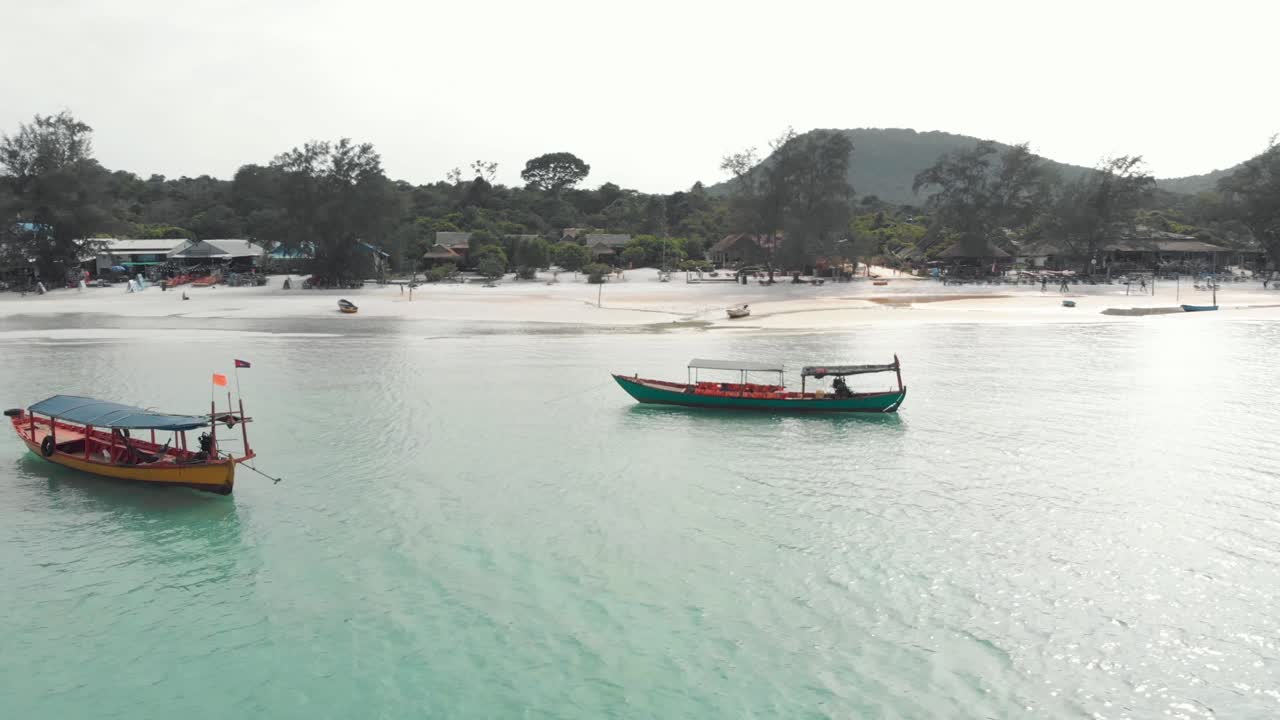 캄보디아 koh rong sanloem에 있는 사라센 베이의 해안선 근처 얕은 바다에 정박해 있는 동남아시아 시골 목조 보트 - 공중 저각 궤도 발사