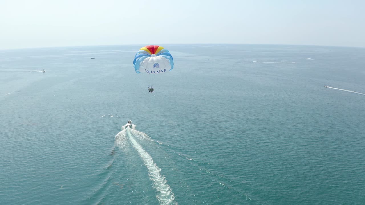 Aerial shot follow speed boat pulling colorful parasail on calm water