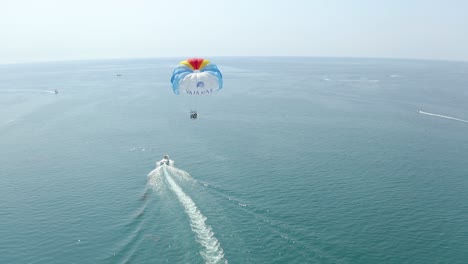 aerial shot follow speed boat pulling colorful parasail on calm water