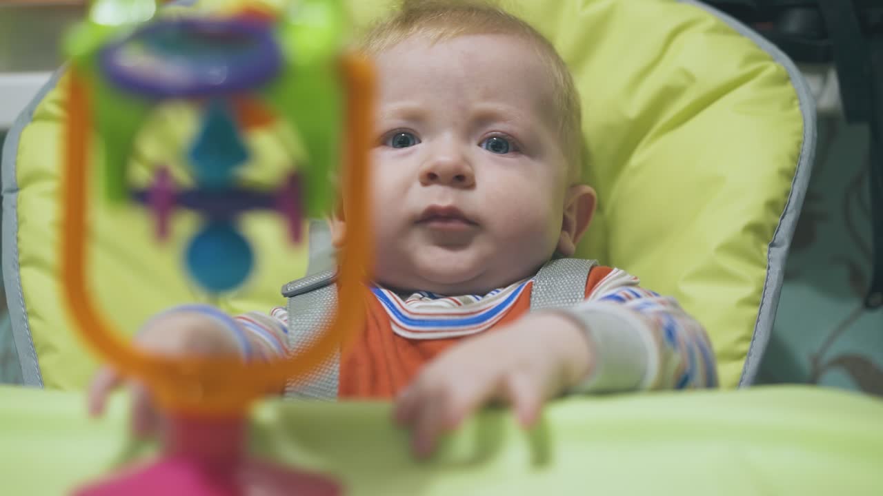little boy tries to take bright toy sitting in highchair