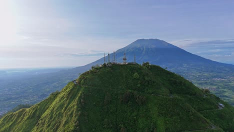 Aerial view of green mountain with tower building on its peak. Mount Telomoyo with Mount Merbabu in the background, Indonesia.