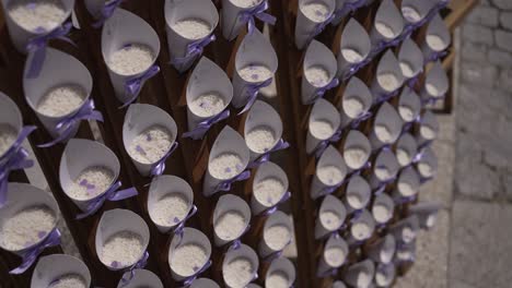 close up of multiple white cones filled with rice and tied with purple ribbons, arranged on a wooden stand