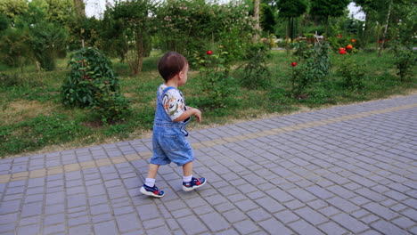 cute caucasian baby boy running by the paved path. toddler runs up to ball and picks it up.