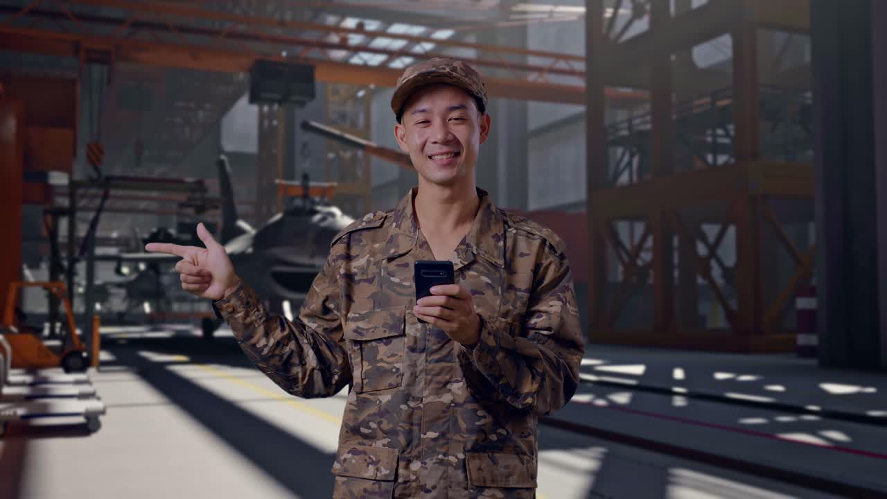 Soldato sorridente in uniforme mimetica che indica qualcosa mentre tiene in mano uno smartphone