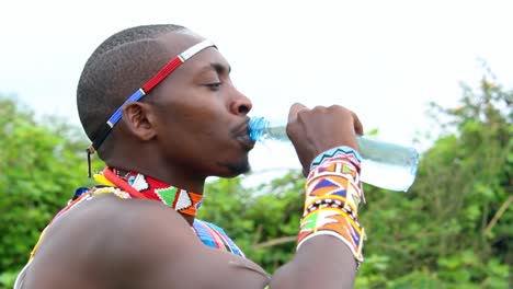 masai man drinking water from a plastic bottle while wearing a traditional maasai clothing