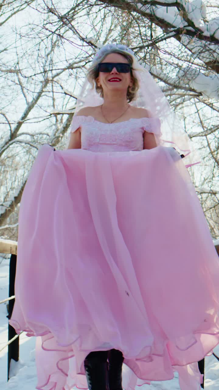 Sposa eccentrica in abito rosa e occhiali da sole cammina in un paesaggio invernale innevato.