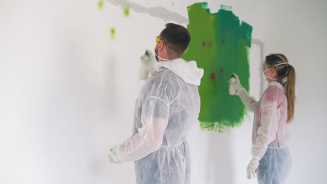 guy and girl in transparent coveralls paint wall with sprays