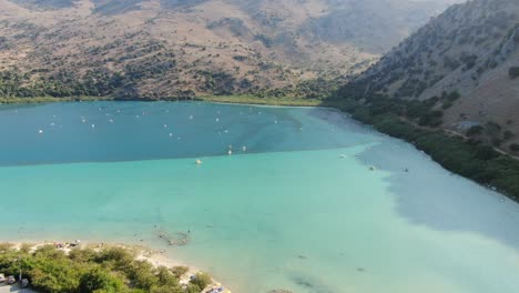 vista de avión no tripulado en grecia volando sobre un lago azul claro y oscuro con pequeños barcos y rodeado de montaña verde en un día soleado en creta