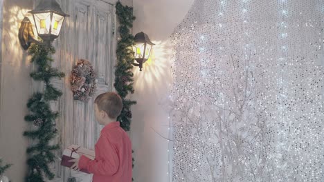 fair haired child holds gift box and knocks on wooden door