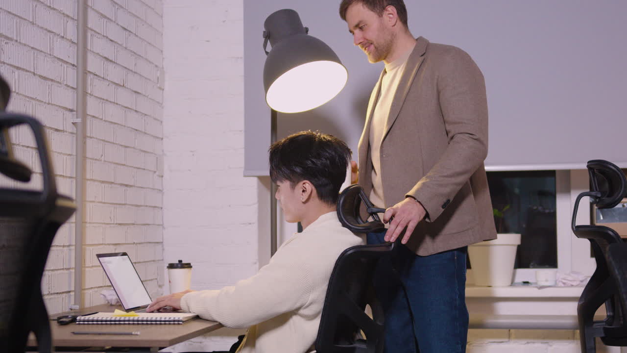 랩톱 컴퓨터에 입력하고 그의 뒤에 서있는 그의 상사와 이야기하는 남성 직원