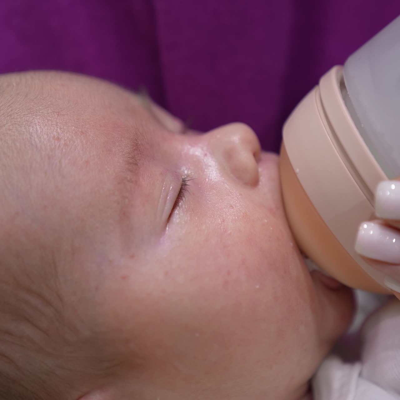 Lovely baby suckling milk from a bottle and slowly closing his eyes. Mother's hand holding a bottle for a baby. Cute baby's face close up