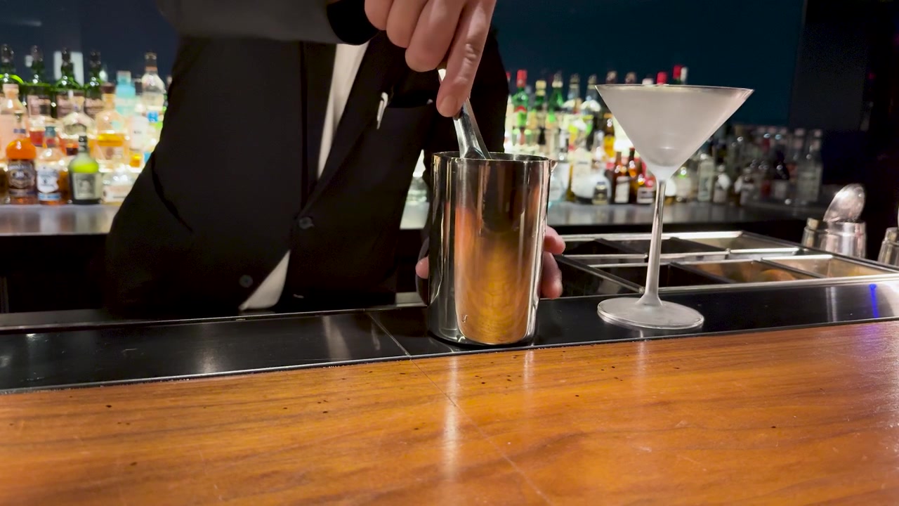 En bartender i sort jakkesæt tilføjer is til en shaker på en trædisk