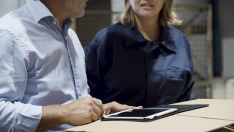 Close-up-of-boss-and-female-employee-talking-in-warehouse,-checking-documents-on-tablet