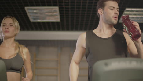 young man drinking water on treadmill in fitness gym.