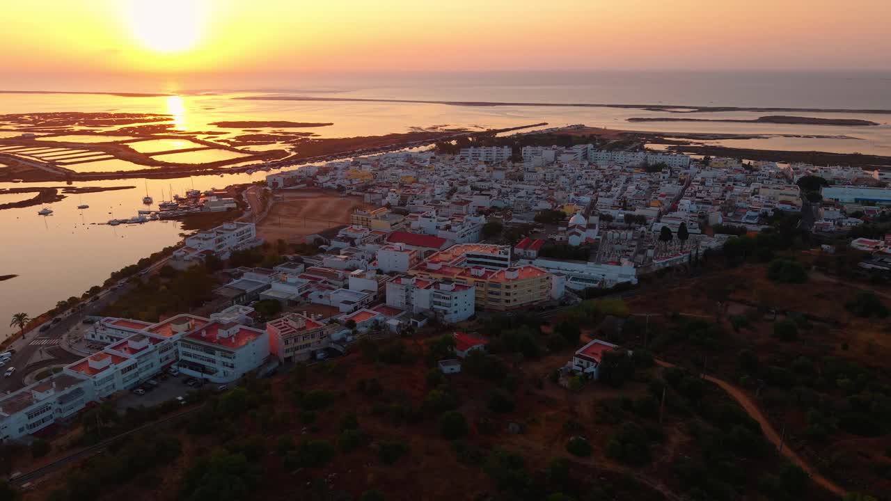 aerial shot above Fustea fishing village at sunrise near Ria Formosa natural park in Algarve region with the village in the foreground and the salt pans in the background, Portugal