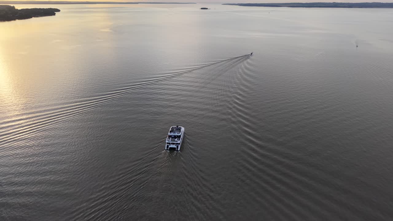 Aerial fly over a catamaran boat crossing wide and calm waters at sunset moment