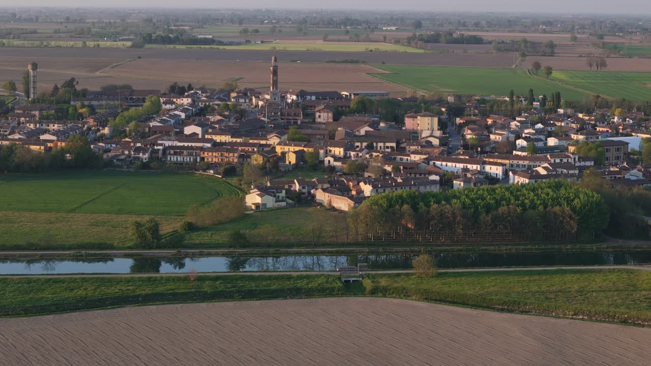 Spinadesco con la torre campanaria centrale della chiesa e un villaggio compatto circondato da campi agricoli, con la SP234 Via Milano che trasporta il traffico lungo il Canale Milano Cremona Po nella Pianura Padana, ripresa statica da drone.