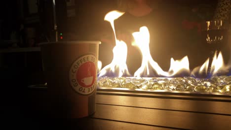 Cierra-El-Café-Humeante-En-Un-Vaso-De-Plástico-De-Diseño-Frente-Al-Fuego