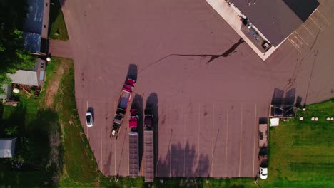 top-down aerial view of a red semi-truck backing up in a rural parking lot beside other parked hopper grain trucks. minnesota, usa