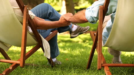 una pareja jubilada sentada en sillas de cubierta tomados de la mano.