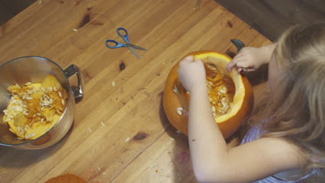 Girl-hollowing-out-a-Halloween-pumpkin,-putting-seeds-in-a-bowl