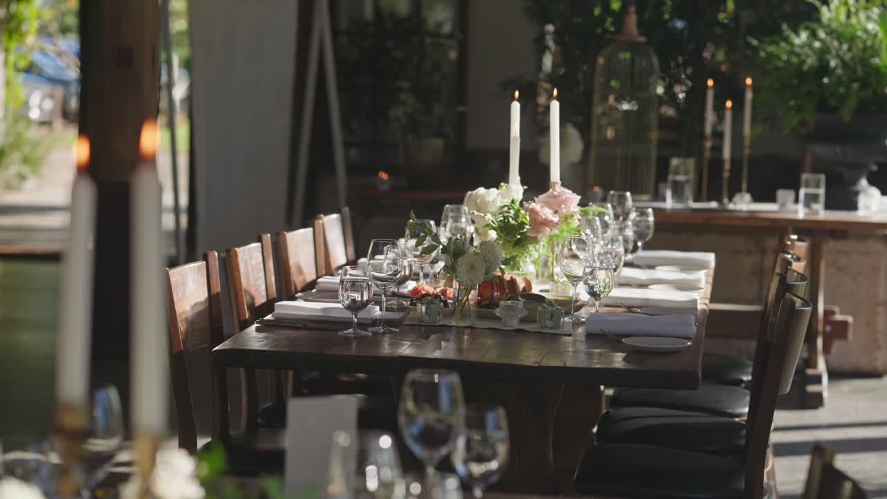 A rustic wooden wedding table setup with burning candles, water goblet, plates, napkins, and cutleries. Cozy and elegant wedding decoration detail