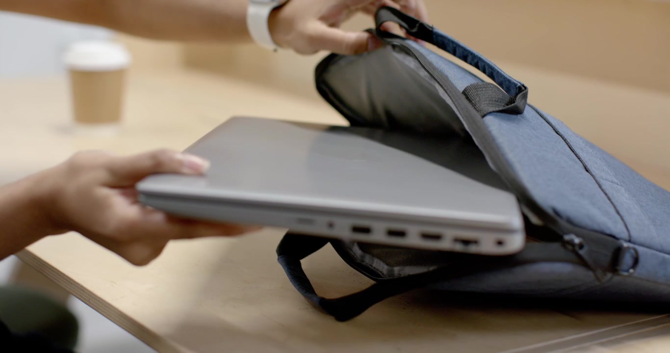 Wanita India mengemas laptop perak dan buku catatan kayu ke dalam ransel setelah minum kopi di kafe