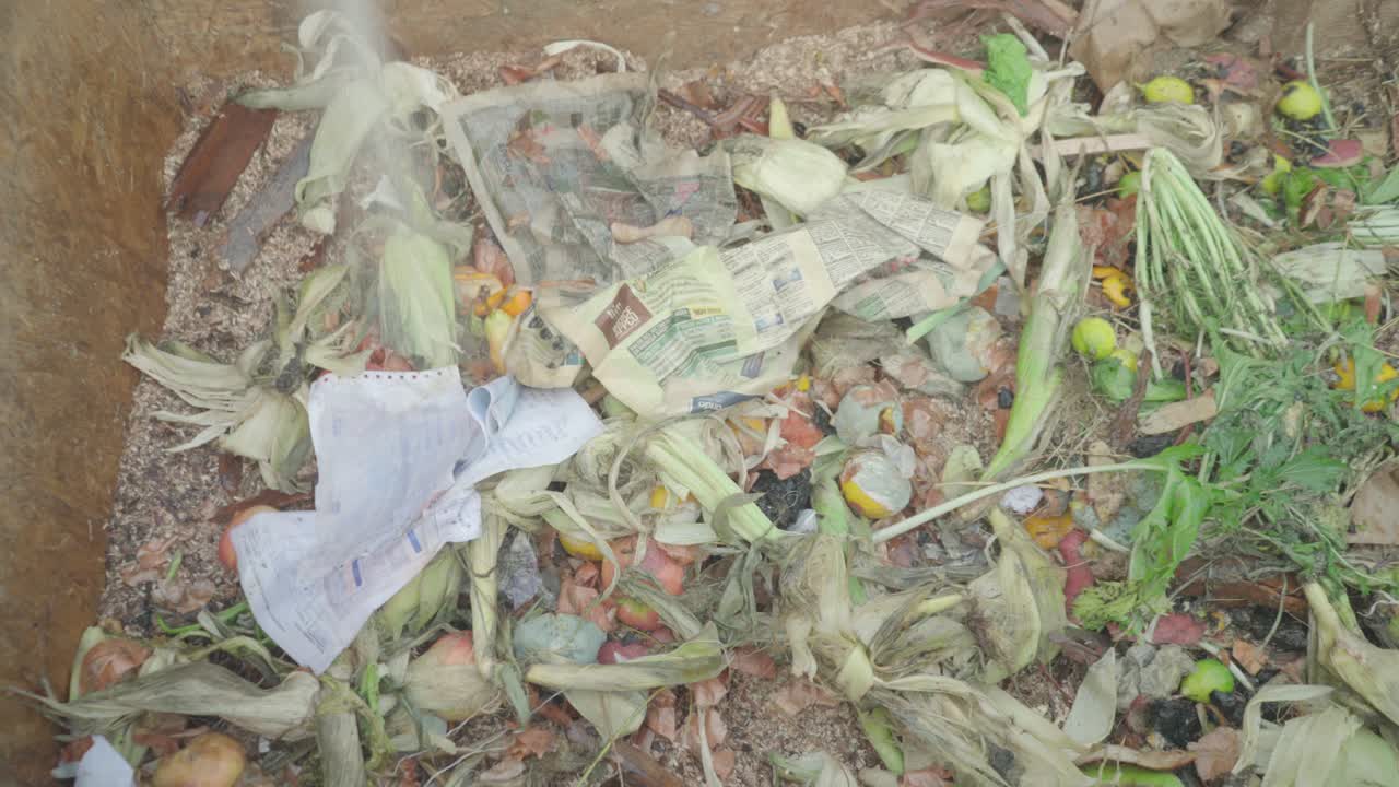 Women prepare a home wooden compost heap box. They add microorganisms to the mixture of organic waste and biodegradable materials.